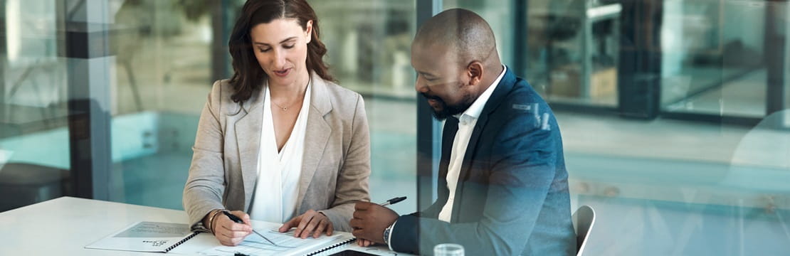 A man and woman looking over papers together at a conference table.
